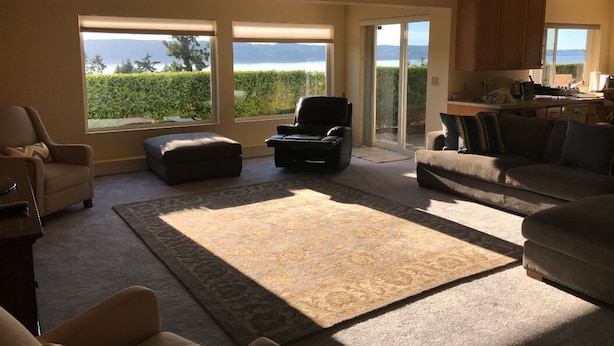 A spacious living room with a large window offering a view of the sea, a fireplace, and a kitchen area.