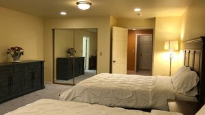 A bedroom with two beds, a dresser, a mirror, and a door leading to another room.