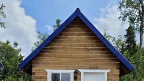 Een klein houten huisje met een blauw dak, een witte deur en een raam.