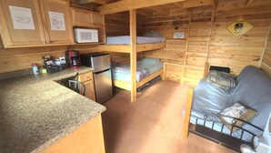 Een compacte kamer in blokhutstijl met stapelbedden, een kitchenette en een zithoekje.