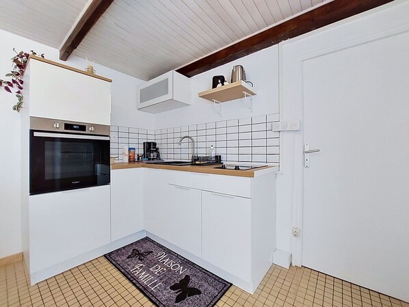 A compact kitchen with white cabinets, a built-in oven, a coffee maker, and a small shelf.