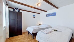 Ein Zimmer mit zwei Betten, Holzboden, einem dunklen Wandschrank und einer Decke mit sichtbaren Balken.