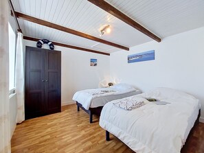 Ein Zimmer mit zwei Betten, Holzboden, einem dunklen Wandschrank und einer Decke mit sichtbaren Balken.