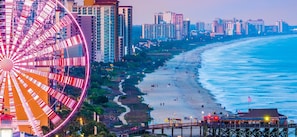 Vista de una playa con una noria grande y edificios altos al fondo.