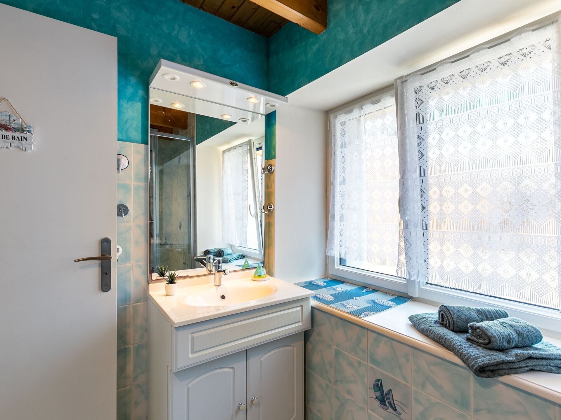 A bathroom with a sink, mirror, and window with lace curtains.