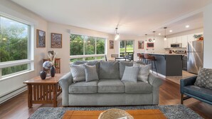 A modern living room with a grey sofa, wooden coffee table, and a view of the kitchen.