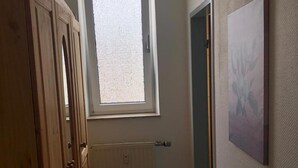 A narrow hallway with wooden flooring, a window with blinds, a radiator, and a door leading to another room. - Hotel Holthausen (Uebach-Palenberg)