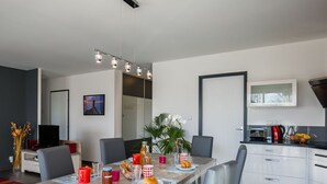 Ein moderner Essbereich mit einem langen Tisch, Stühlen und einer Küche im Hintergrund.