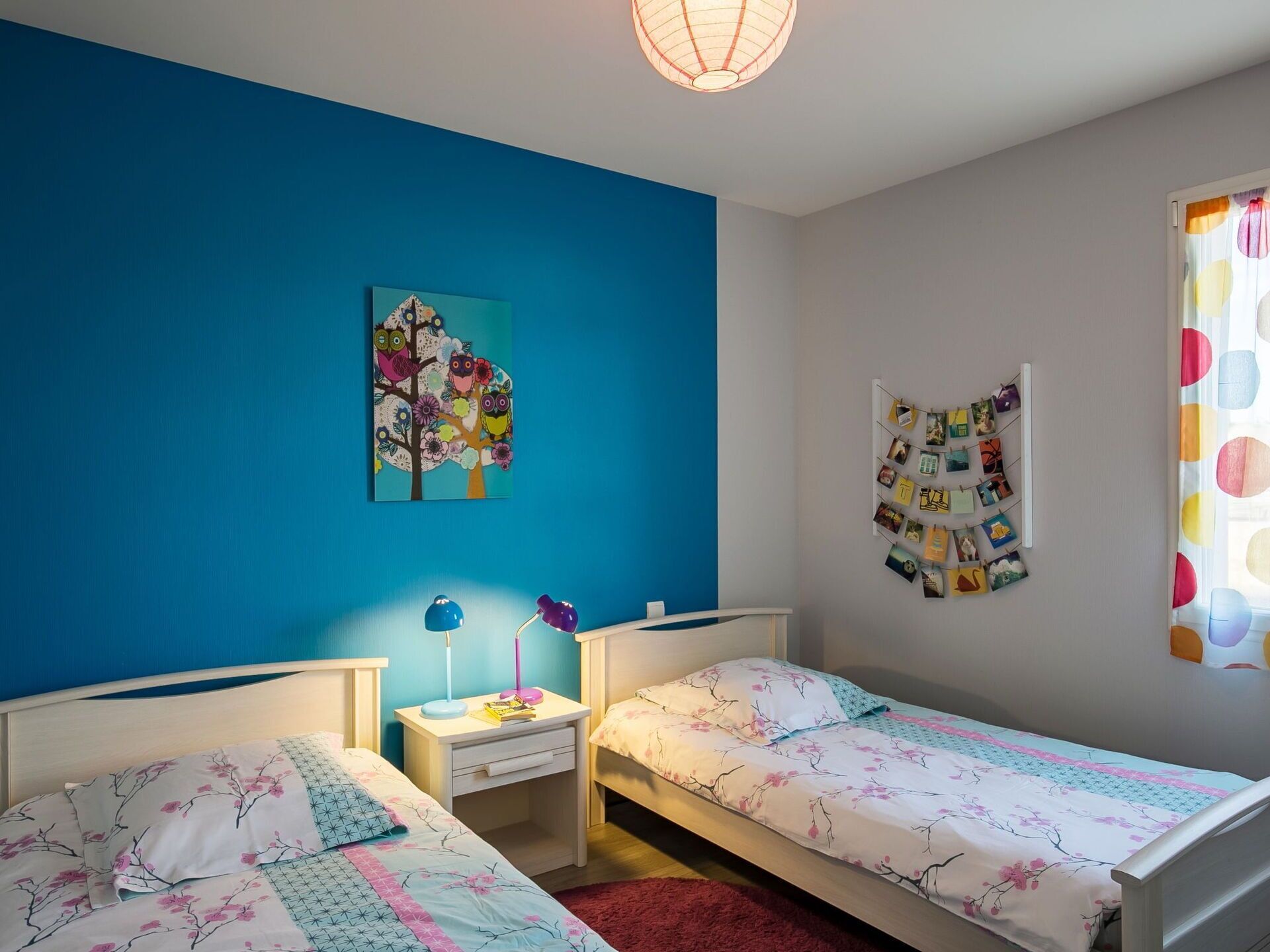 Ein Schlafzimmer mit zwei Betten, einem Nachttisch, einer Wand mit einem farbenfrohen Gemälde und einer Pinnwand mit Fotos.