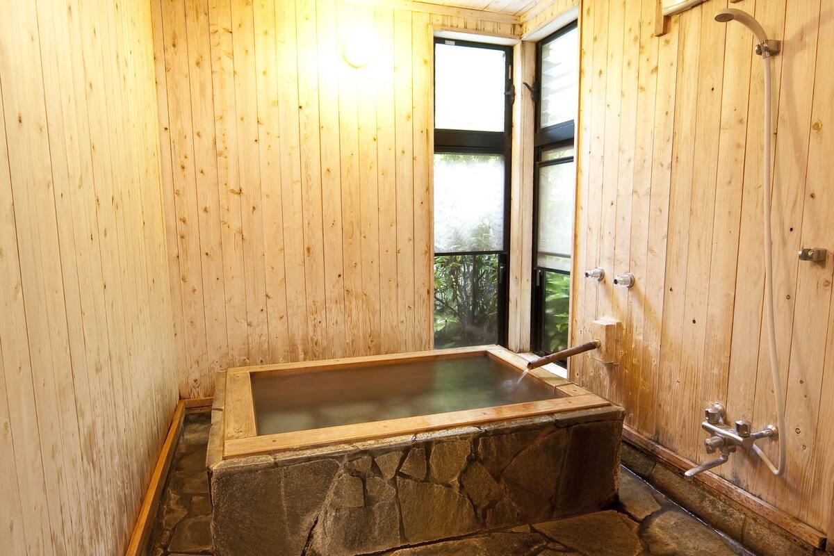 A stone hot tub in a wooden room with a window and a shower.