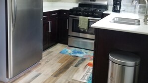 Una cocina con armarios de madera oscura, electrodomésticos de acero inoxidable, un salpicadero de azulejos y una alfombra estampada.