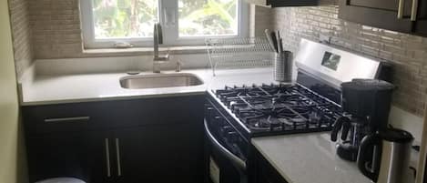 A compact kitchen with dark cabinets, a stainless steel stove, a microwave, and a window with a view of greenery.