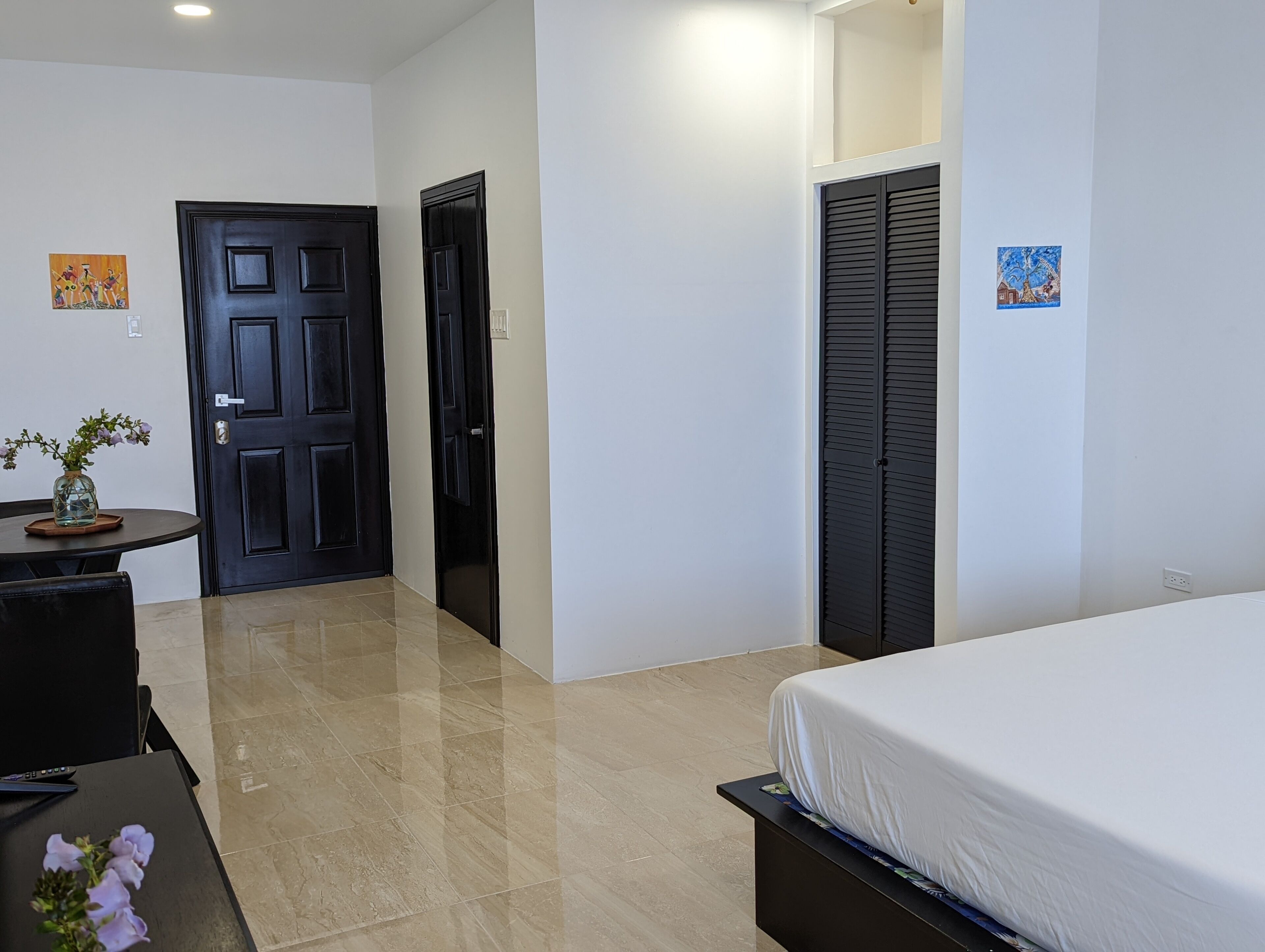 Hotelkamer met een bed, een tafeltje met een bloevas, een deur en een muur met twee foto's.