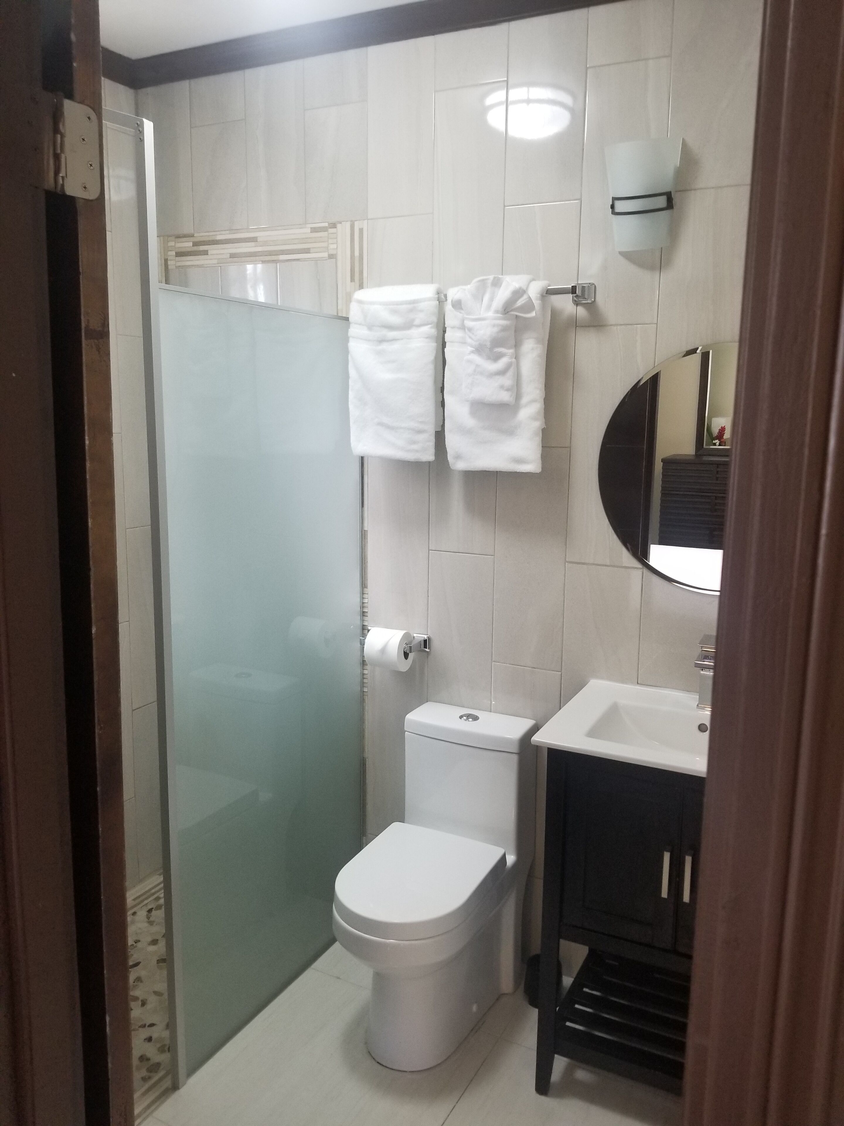 Un baño pequeño con cabina de ducha de vidrio, inodoro, lavamanos y espejo.