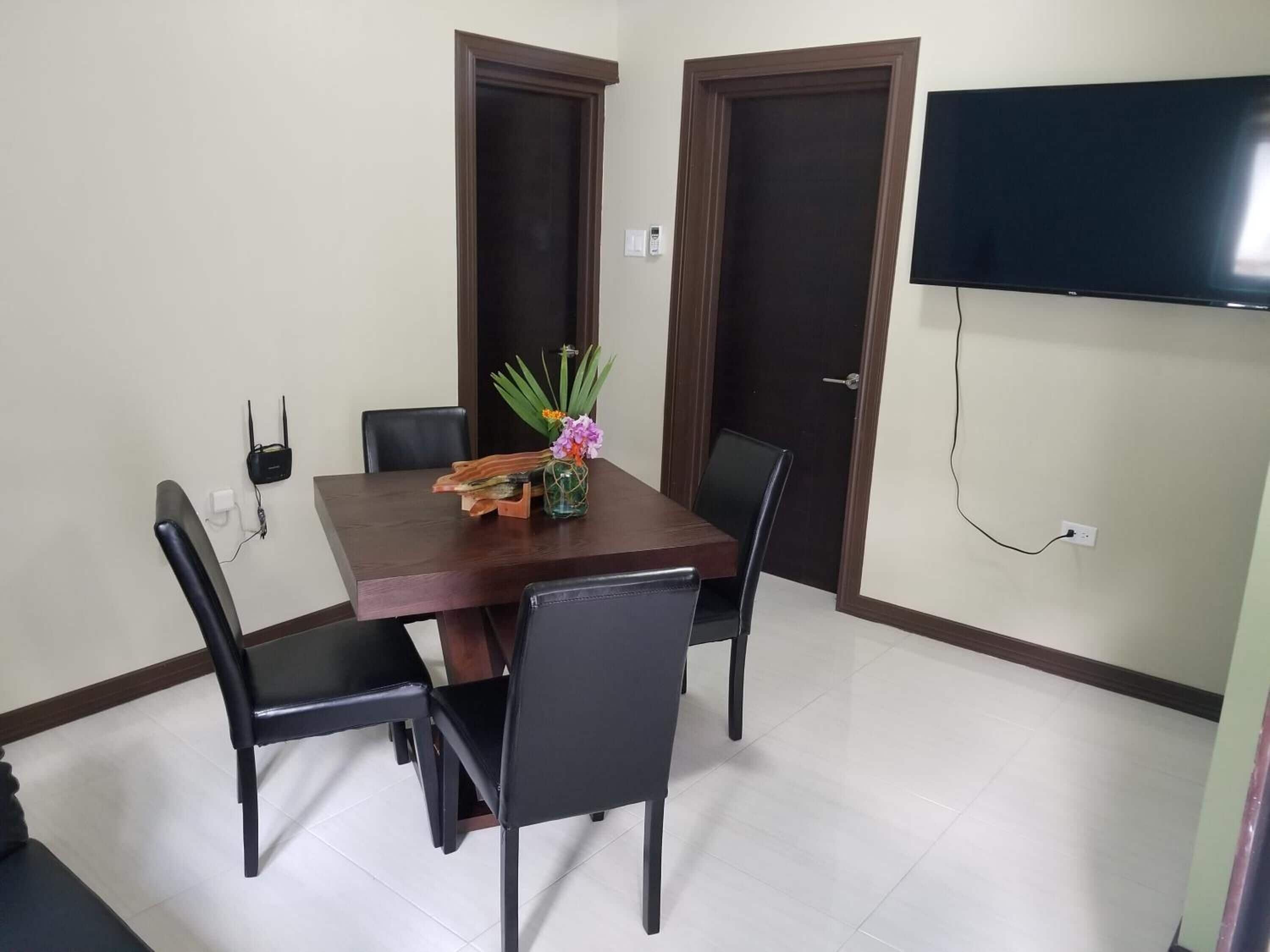A dining area with a wooden table, four chairs, and a TV mounted on the wall.