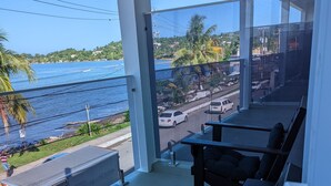 Un balcón con vistas al mar y a una carretera. Hay sillas y una mesa en el balcón.