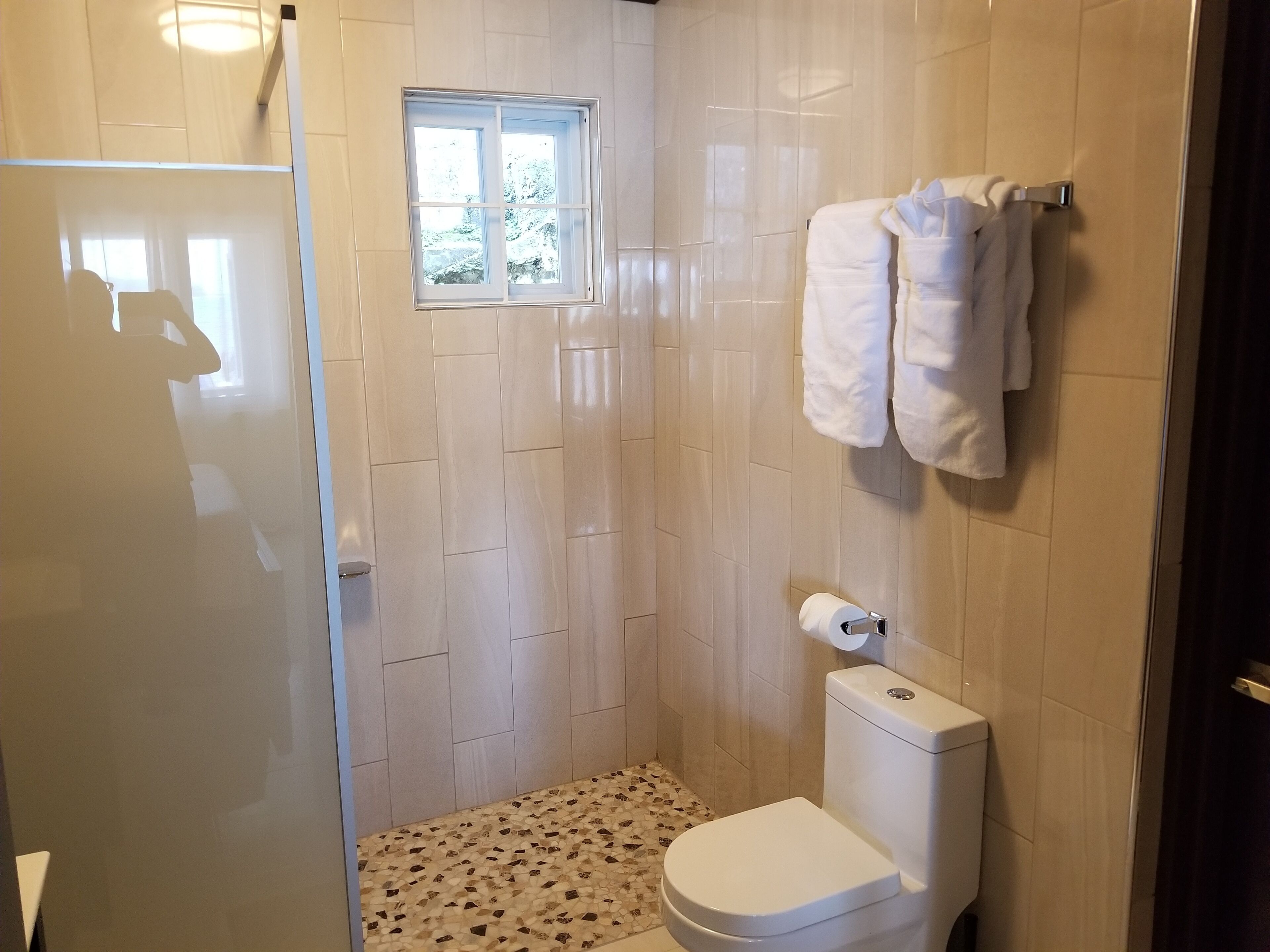 Casa de banho pequena e revestida a azulejos, com sanita, janela e um porta-toalhas.