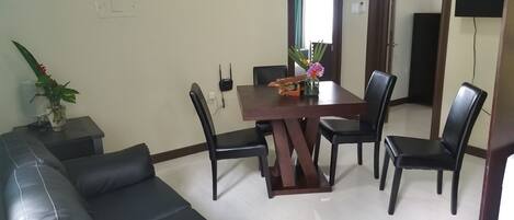 A dining area with a wooden table and chairs, a black leather sofa, and a small side table with a plant.