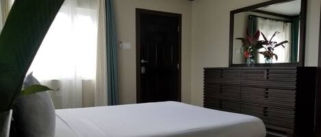 A bedroom with a bed, a dresser, a mirror, and a window with curtains.