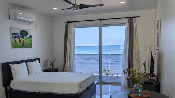 Un dormitorio con cama, escritorio, silla, mesa y vista al mar.