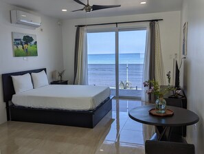 Quarto com cama, escrivaninha, cadeira, mesa e vista para o mar.