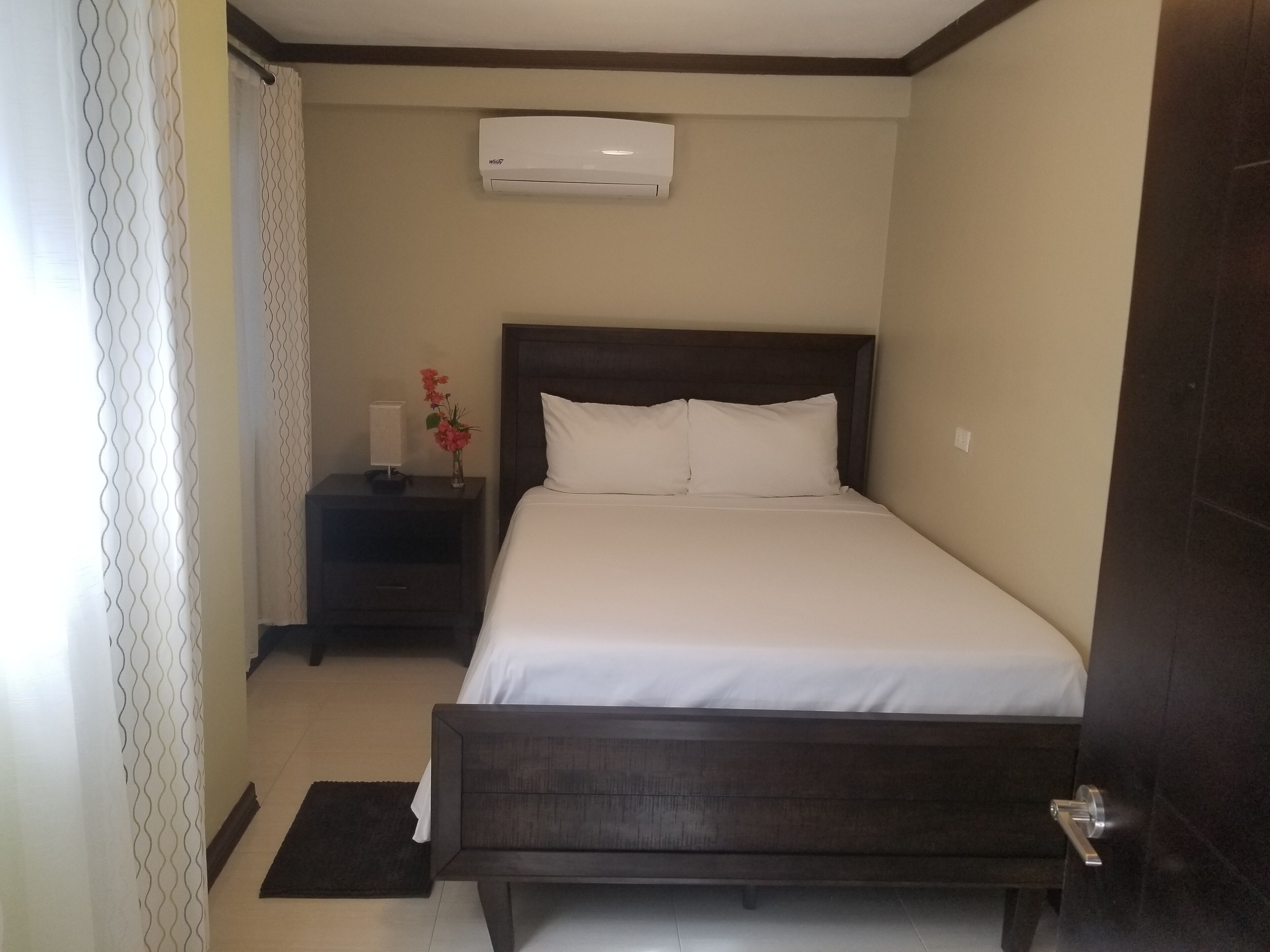 A hotel room with a bed, a nightstand, a wall-mounted air conditioner, and a door.