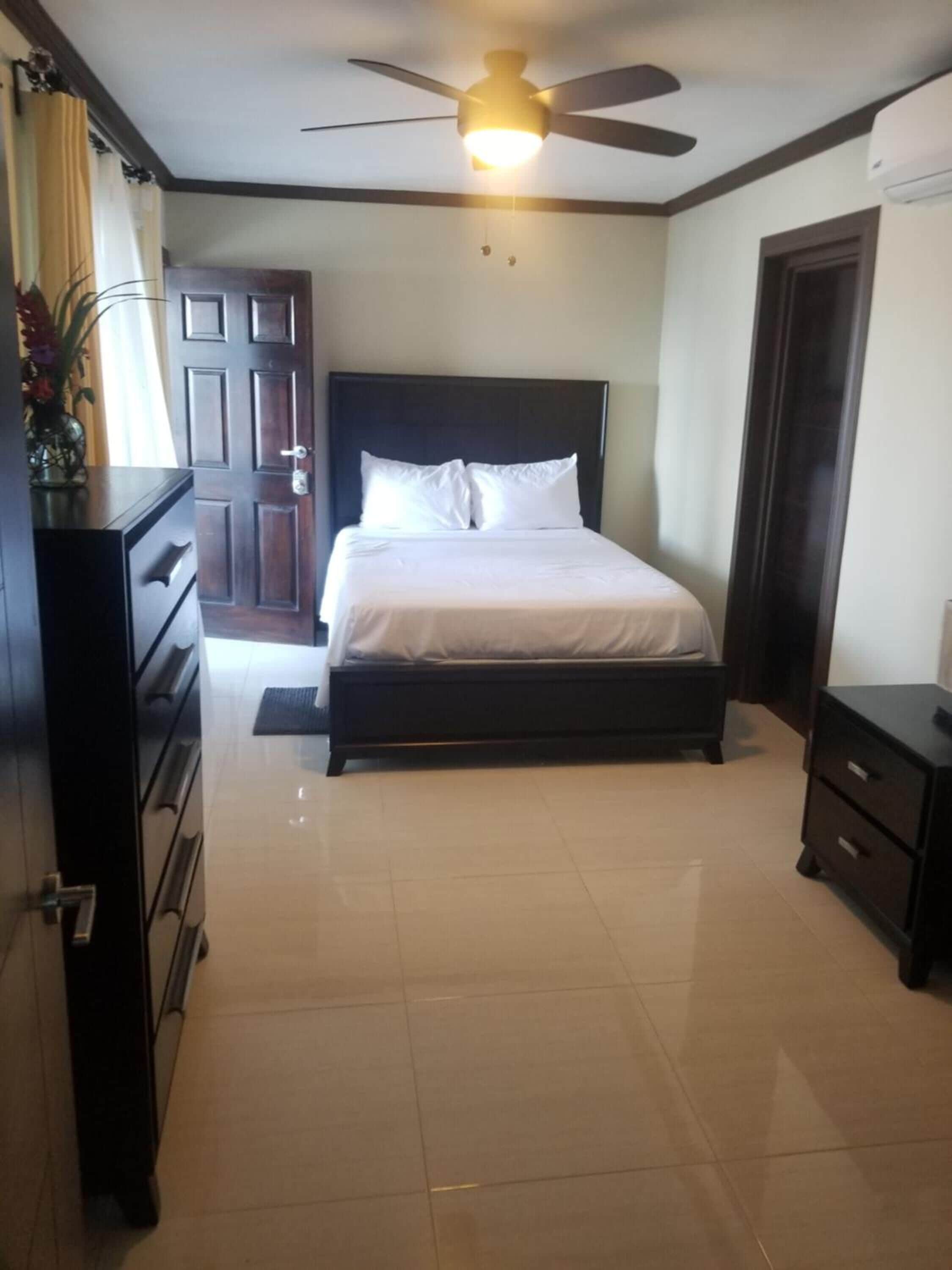 A bedroom with a bed, a ceiling fan, a dresser, and a door.