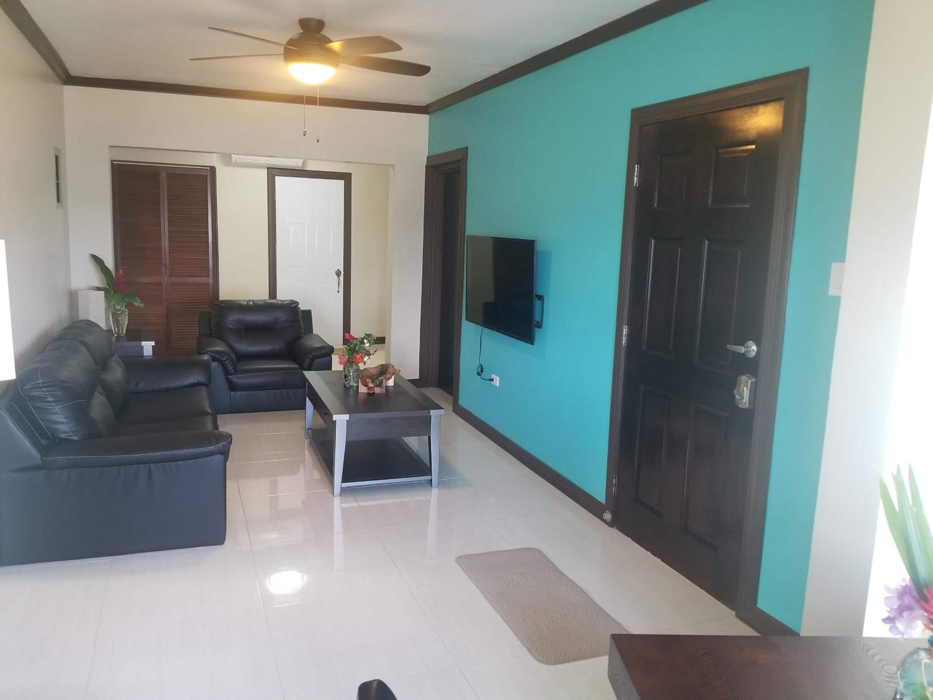 A living room with a black leather sofa, a coffee table, and a TV mounted on the wall.
