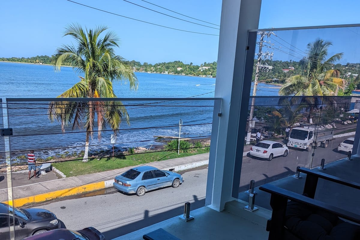 A balcony with a view of a beach and the sea, featuring a table and chairs.