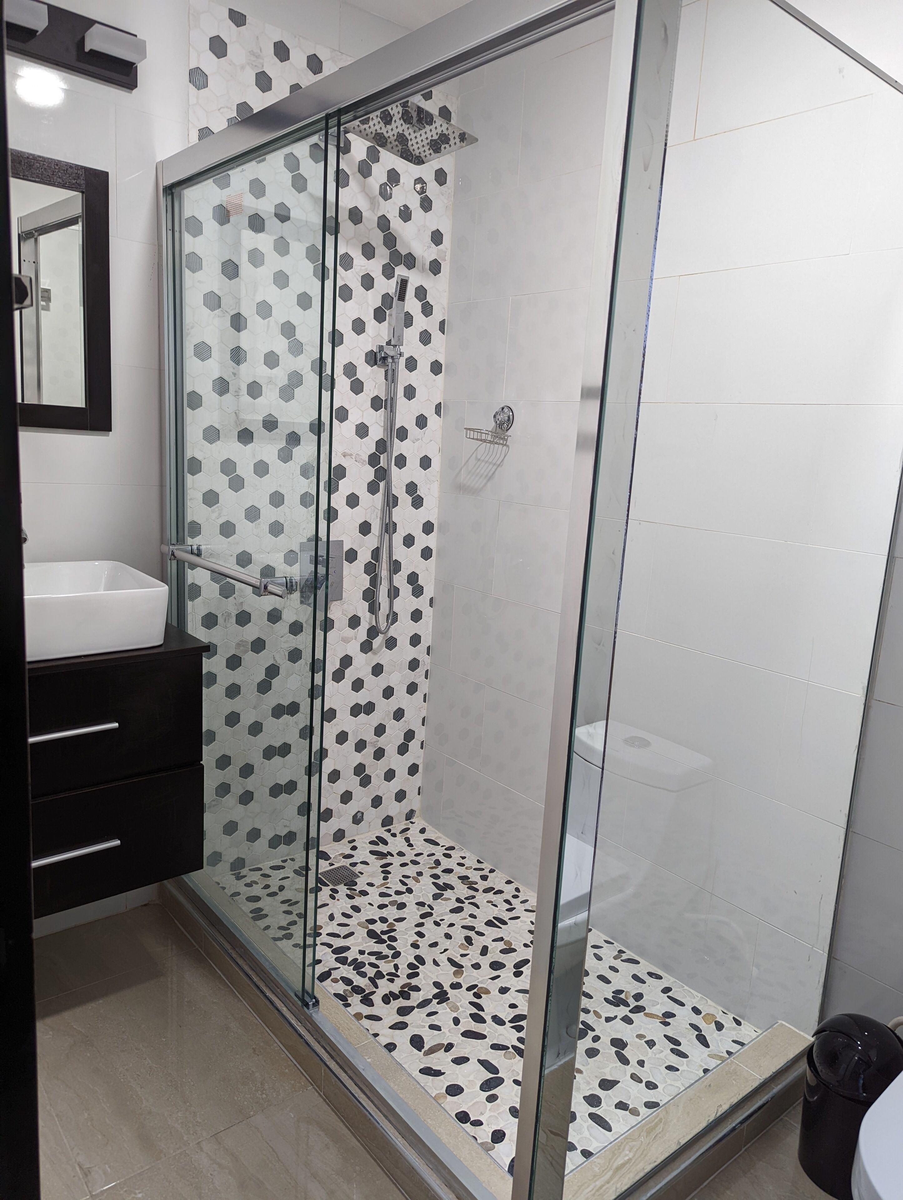 A modern bathroom with a glass-enclosed shower, a white sink, and a black vanity.