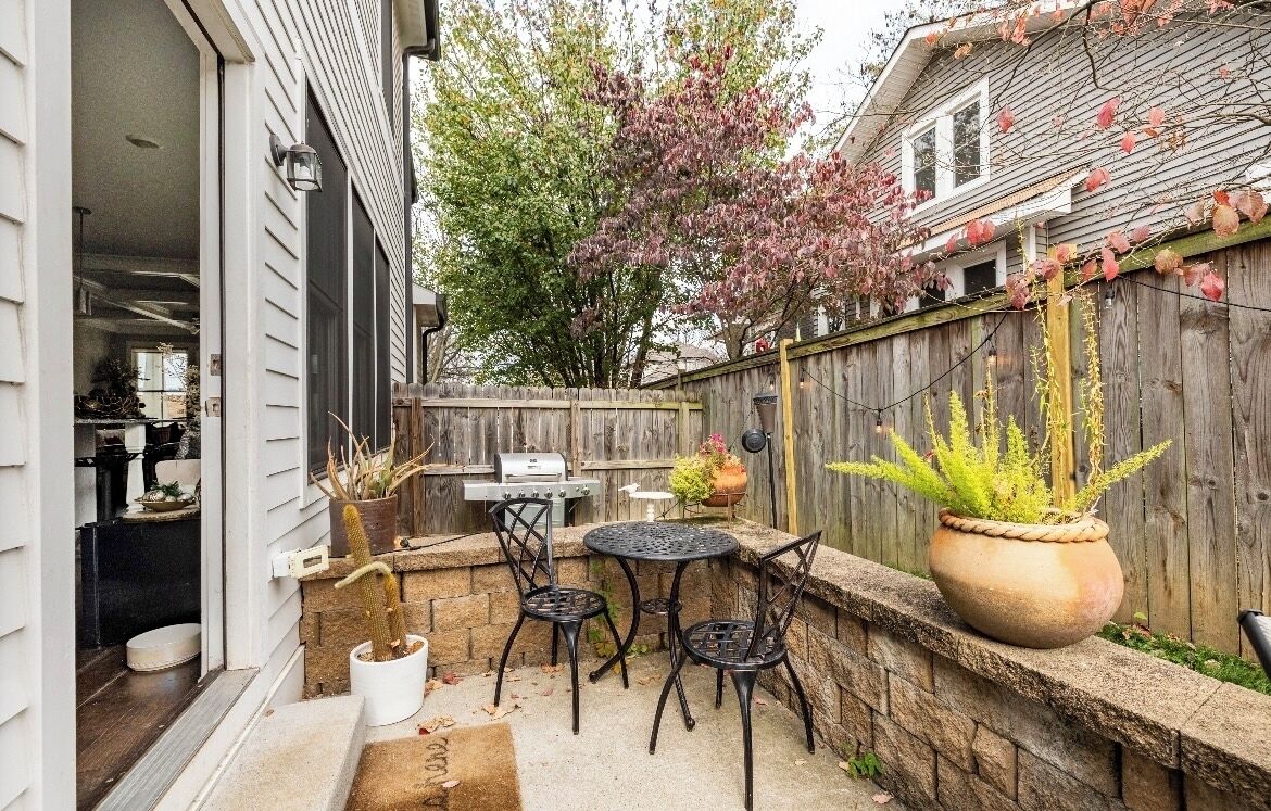 A backyard with a barbecue grill, two metal chairs, a potted plant, and a wooden fence.