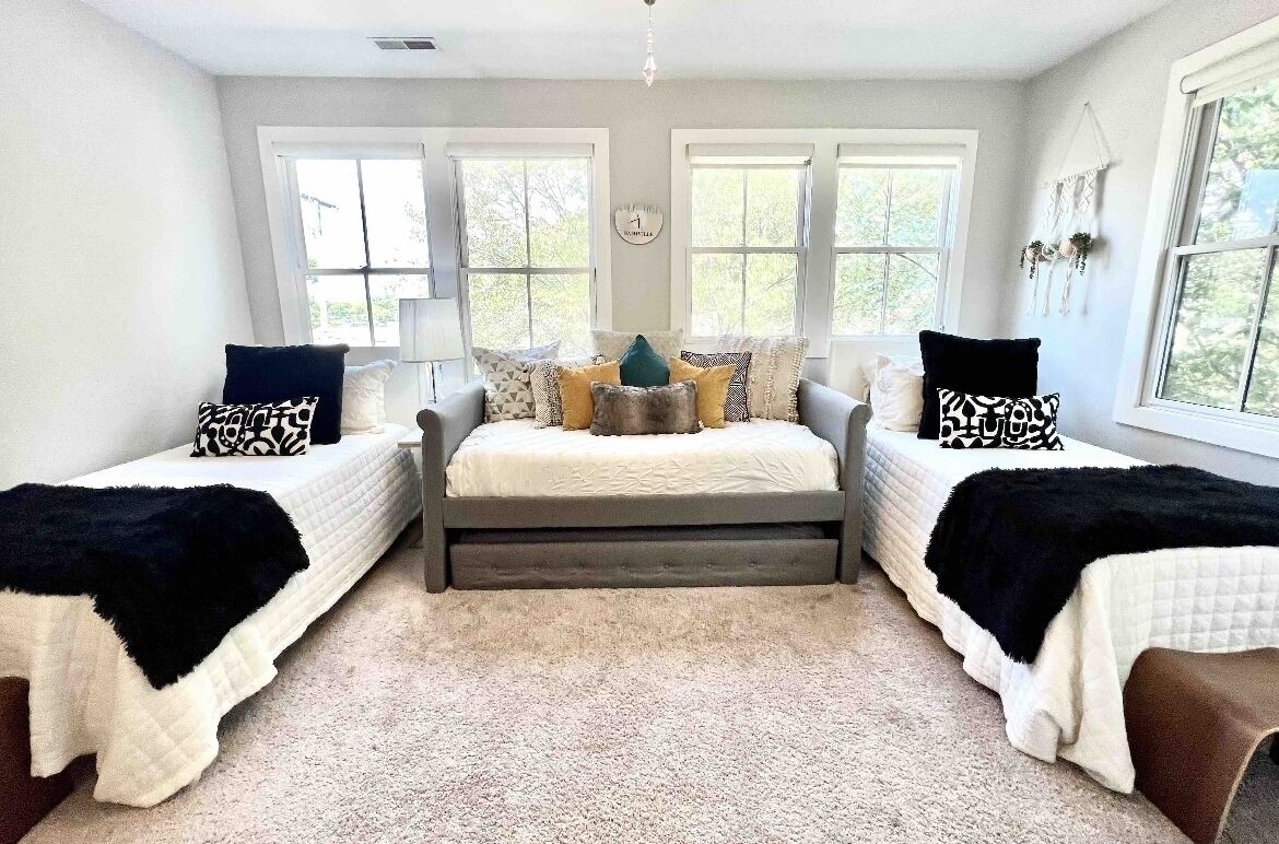 A bedroom with two single beds, a central bed, and a window with a view.