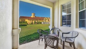 Un portico riparato con due sedie e un tavolo, con vista su un prato curato e un edificio con tetto rosso.