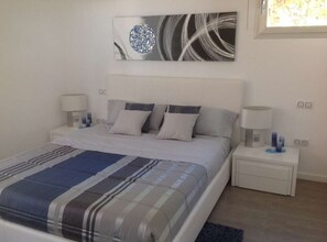 Un dormitorio con cama, dos mesitas de noche, un cuadro en la pared y una ventana.