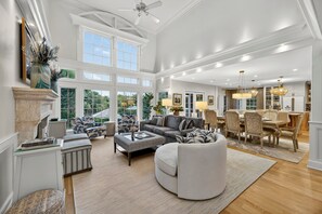 A spacious living room with a fireplace, large windows, a dining area, and a chandelier. - Spacious Luxury Home! Private POOL and GOLF Course Views! (Kiawah Island)
