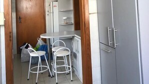 Een keuken met witte kastjes, een koelkast en twee witte barkrukken.