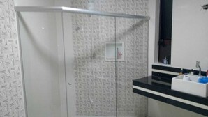 Een badkamer met een witte, gestructureerde wand, een glazen douchecabine, een zwart aanrecht en een witte wastafel met een spiegel erboven.