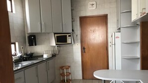 Een kleine keuken met witte kastjes, een magnetron, een koelkast en een eethoekje met twee witte stoelen.