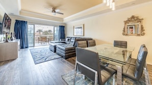 A spacious living room with a glass dining table, leather sofas, and a ceiling fan. - Here's to New Memories!  Luxury Condo near Disney with Resort Access! (Kissimmee)