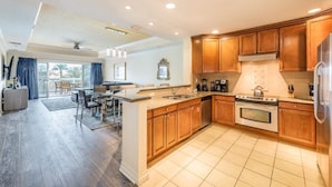 A modern kitchen with wooden cabinets, a stainless steel refrigerator, and a large island with a sink. - Here's to New Memories!  Luxury Condo near Disney with Resort Access! (Kissimmee)