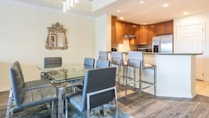 A modern kitchen with wooden cabinets, a stainless steel refrigerator, and a glass dining table with chairs. - Here's to New Memories!  Luxury Condo near Disney with Resort Access! (Kissimmee)