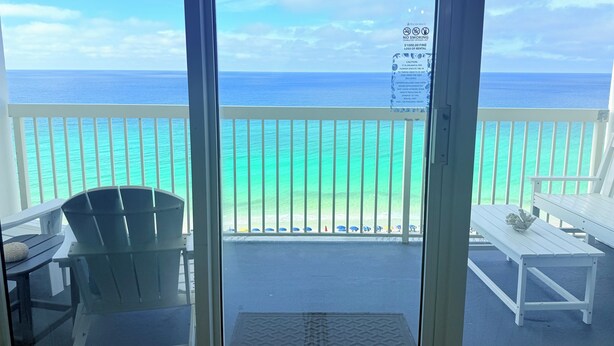 A balcony with a view of the ocean, a white chair, a white bench, and a no-smoking sign.