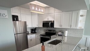 A modern kitchen with white cabinetry, stainless steel appliances, a granite countertop, and a bar stool area.