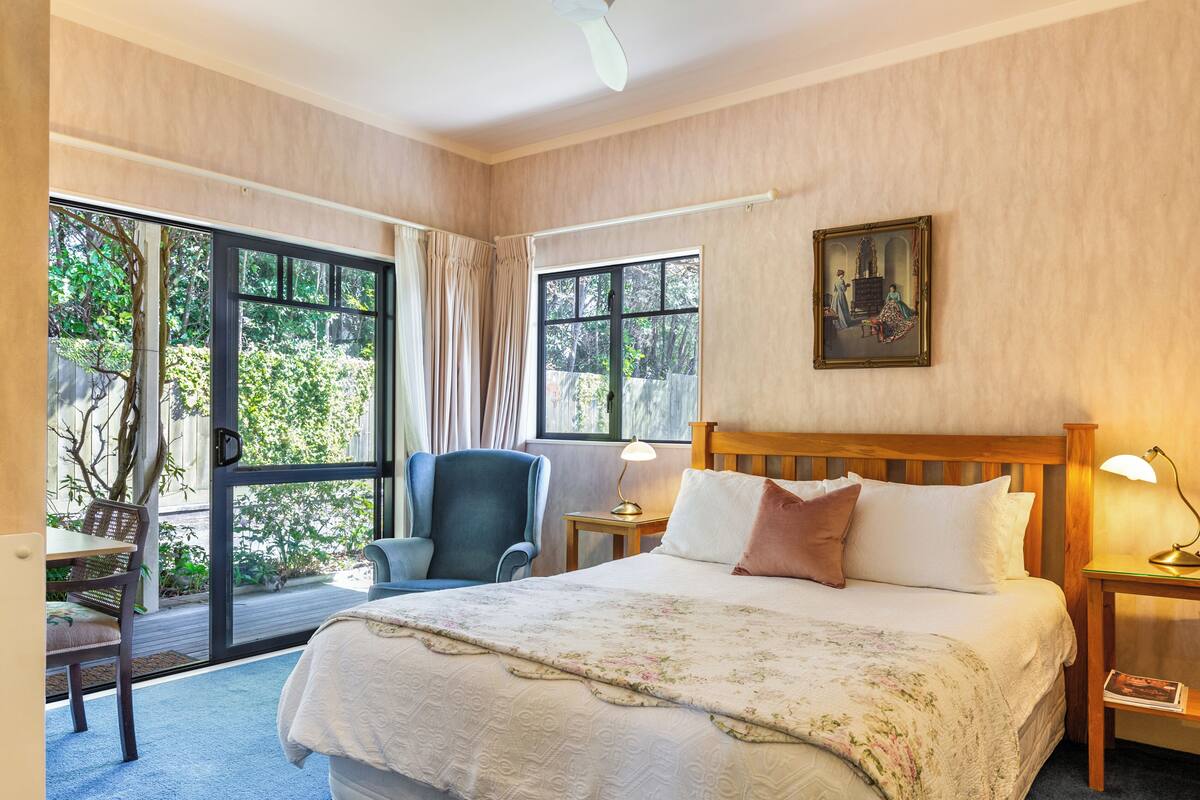 A bedroom with a large bed, two bedside tables with lamps, a chair, and a window with curtains.