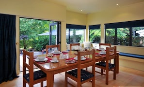 A dining area with a wooden table set for four, large windows with views of greenery, and a door leading outside. - Olive Rabbit - Boutique Bed & Breakfast (Turangi)