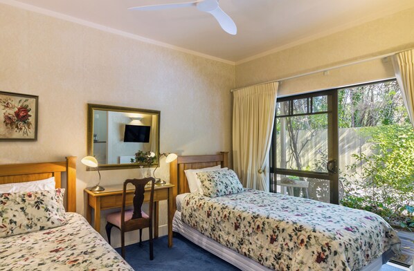 A hotel room with two beds, a desk with a chair, a ceiling fan, and a window with curtains.