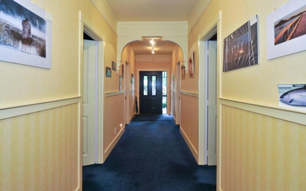 A hallway with cream-colored walls, a dark carpet, and framed pictures on the walls.