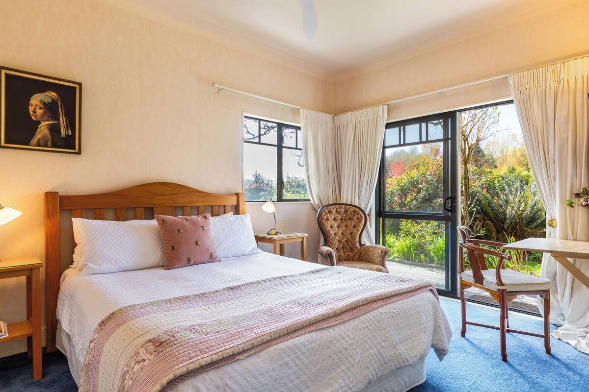 A bedroom with a large bed, a chair, a table, and a view of the outdoors.