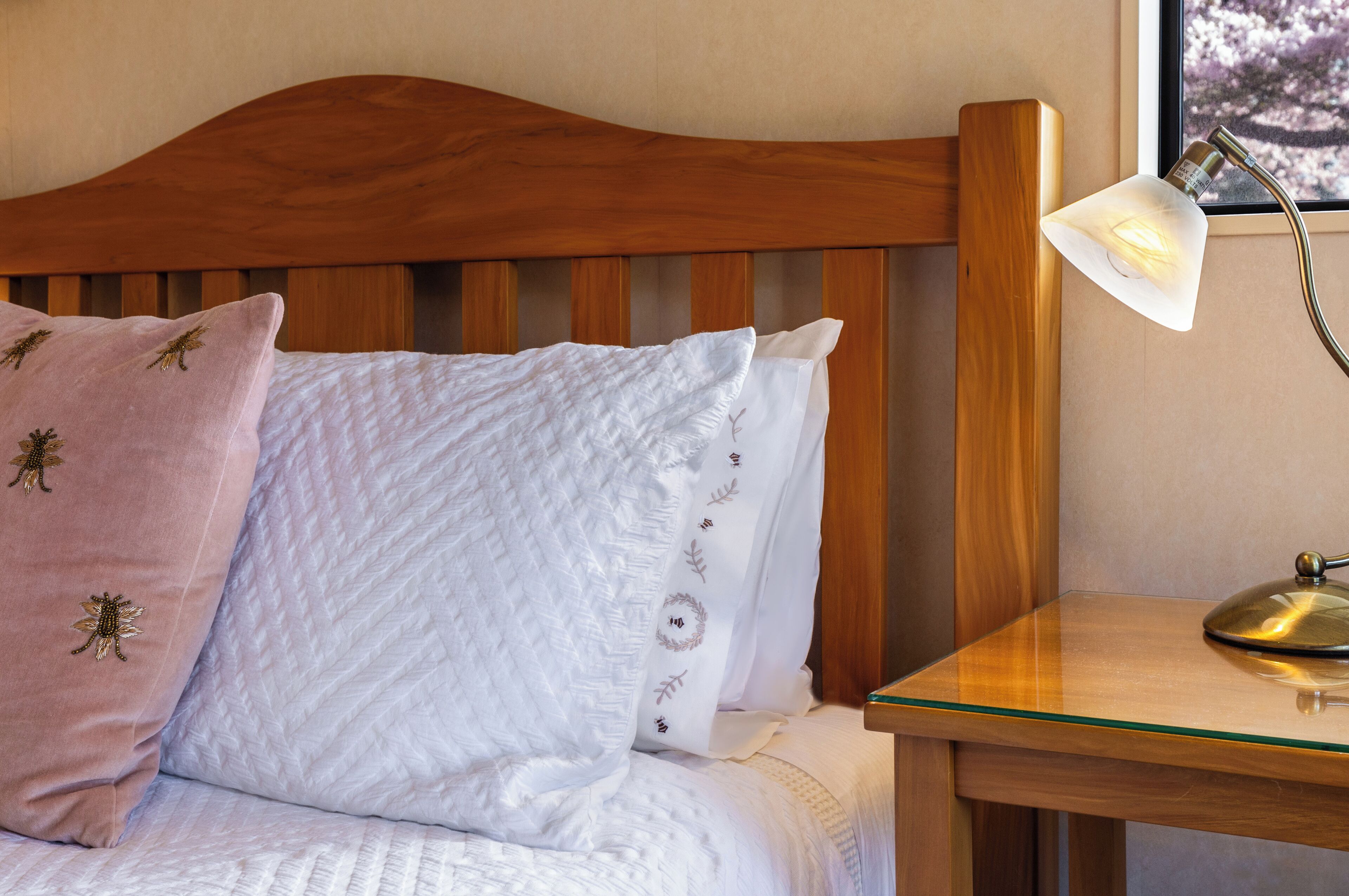 A bed with wooden headboard, white and pink pillows, and a bedside table with a lamp.
