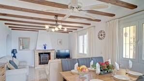 A spacious living room with a wooden ceiling, a fireplace, a television, and a dining area set for a meal. - La Repere by Interhome (Benissa)